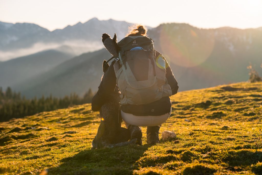 Person kniet mit Hund im Abendlicht am Sudelfeld bei Bayerischzell, Fotowanderung mit Hund in alpiner Landschaft